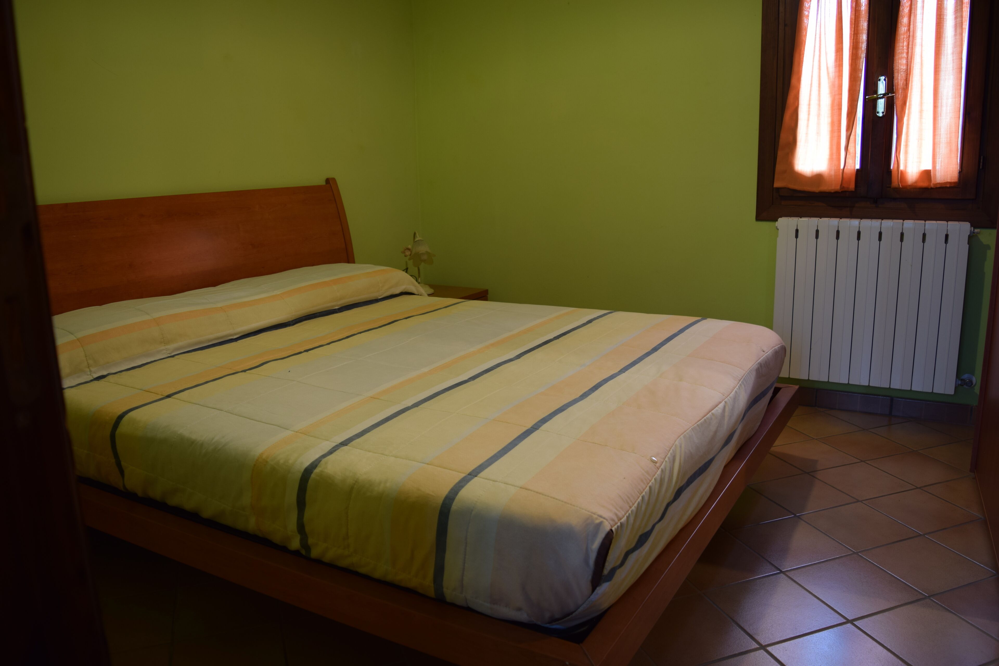 Una cama individual con cabecera de madera en una habitación con paredes verdes y una ventana con cortinas.