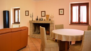 Ein Wohnzimmer mit Kamin, einer Couch, einem Esstisch mit Stühlen und einem Fenster mit Vorhängen.