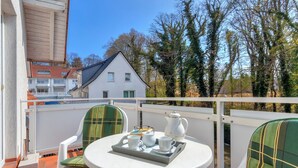 A balcony with a white table and chairs, a tray with cups and a teapot, and a view of a white house and trees. - Hansehus, Whg. 5: close to the beach in Zinnowitz with balcony and WLAN (Zinnowitz)