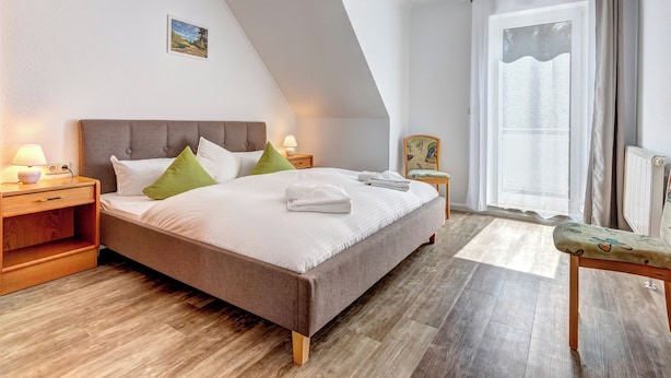 A bedroom with a large bed, wooden flooring, a nightstand with a lamp, and a window with curtains. - Hansehus, Whg. 5: close to the beach in Zinnowitz with balcony and WLAN (Zinnowitz)