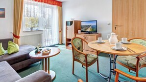 Een gezellige kamer met een bank, een klein tafeltje, een eettafel met stoelen, een televisie en een raam met gordijnen.