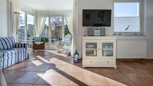 A living room with a sofa, a TV, a cabinet, and a window with a bird.