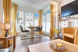 Habitació d'hotel amb taula de menjador, dues cadires, un sofà, un televisor i una finestra amb cortines.