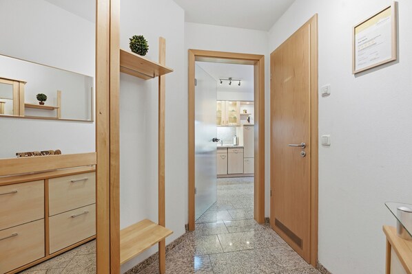 Un pasillo con un banco de madera, un espejo y una puerta que da a una zona de cocina.