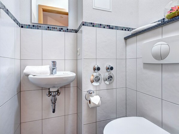 Un baño con lavamanos blanco, inodoro y ducha con panel de control.