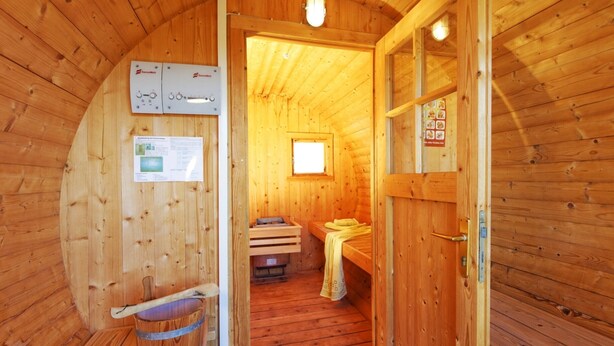 Uma sala de sauna de madeira com um banco, um balde e uma pequena janela.