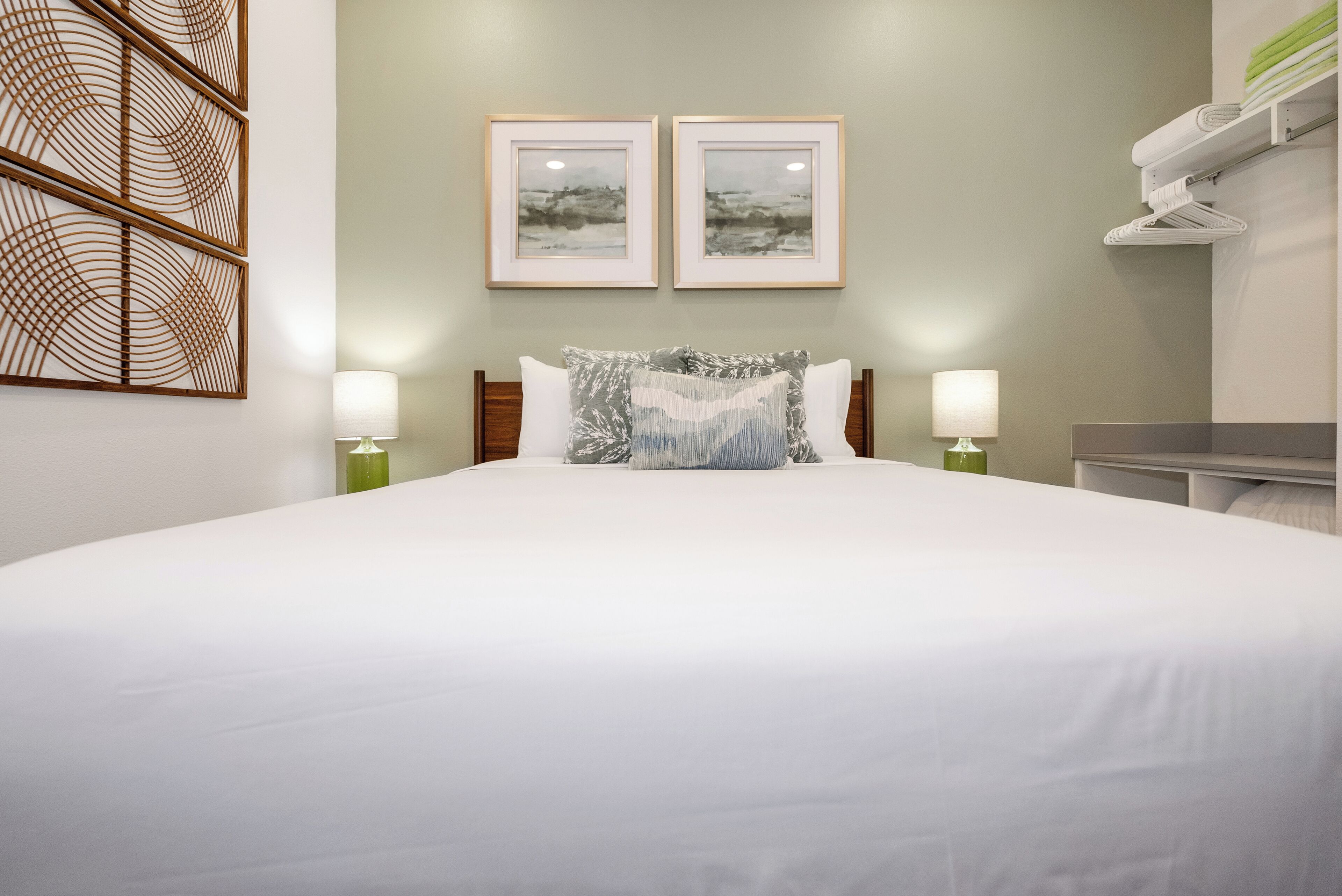 A neatly made bed with white linens, two framed pictures on the wall, and two bedside lamps.