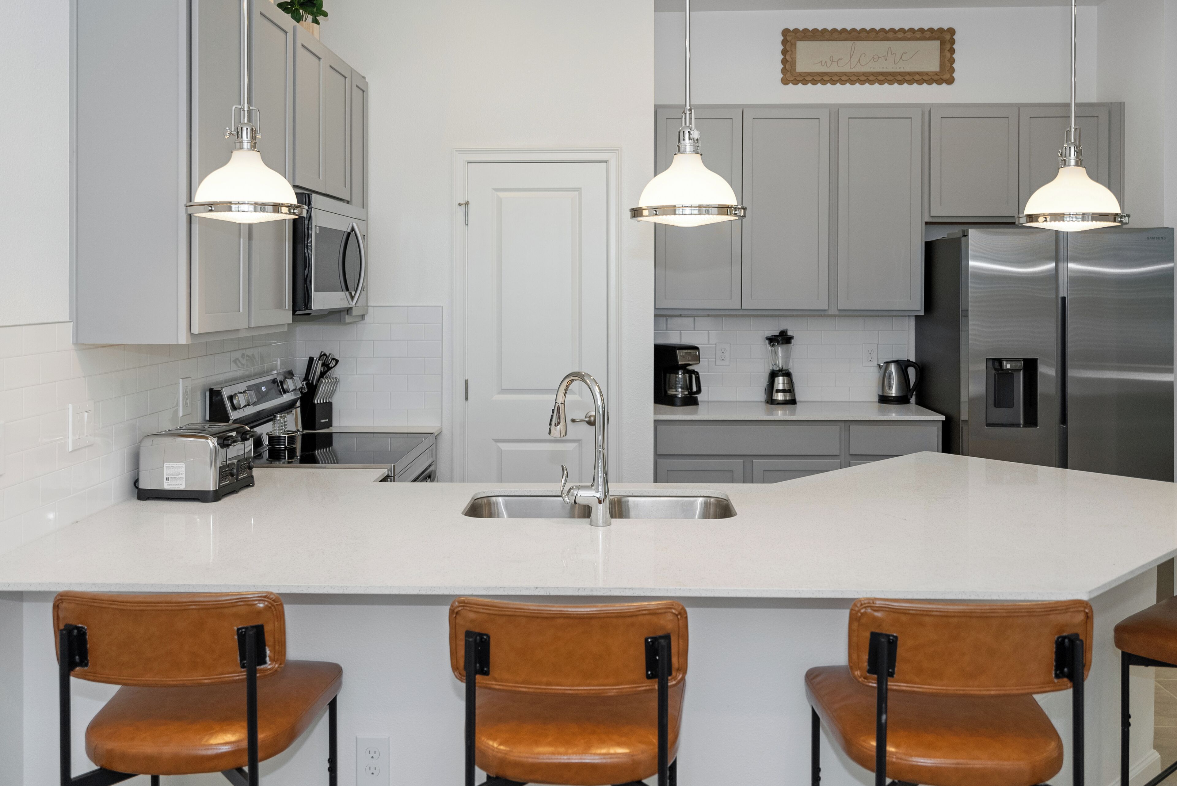 A modern kitchen with a large island, stainless steel appliances, and pendant lighting.