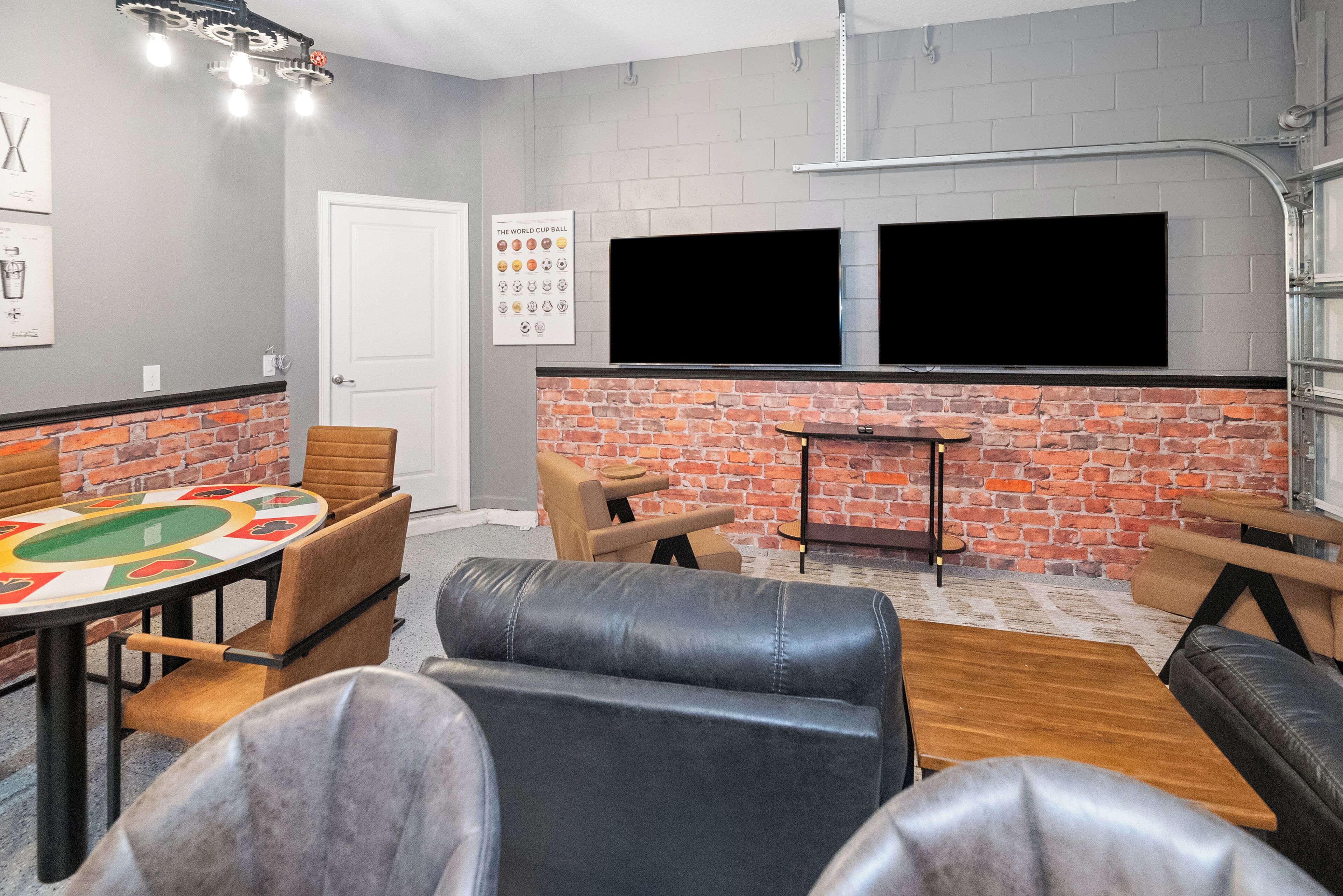 A room with a brick wall, two TVs mounted above it, leather seating, and a small table.