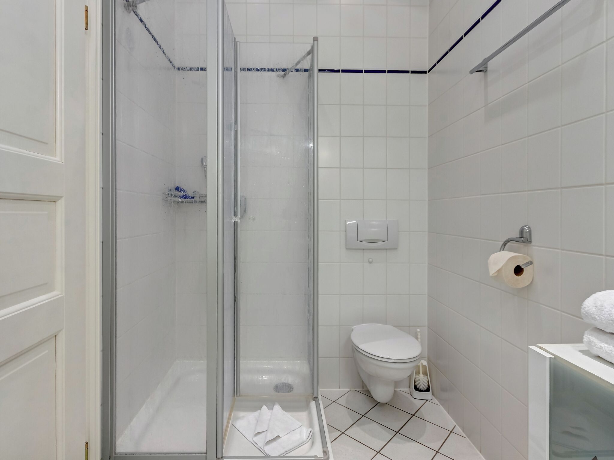 Un baño moderno con cabina de ducha de vidrio, inodoro y lavamanos con una pila de toallas.