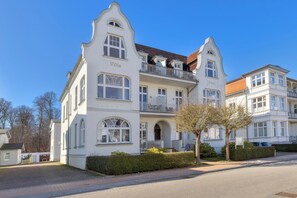A white, two-story villa with a balcony, a nameplate reading "Villa Friede," and a small garden area.