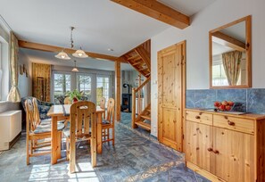 Un comedor amplio con sillas y mesa de madera, una escalera de madera y un piso de baldosas de piedra.