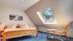 Une chambre avec un plafond en pente, une lucarne, un lit, une chaise et une petite table.