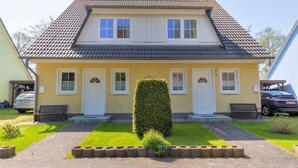 Une maison à deux étages, avec un toit en tuiles, un porche à l’avant et une pelouse bien entretenue.