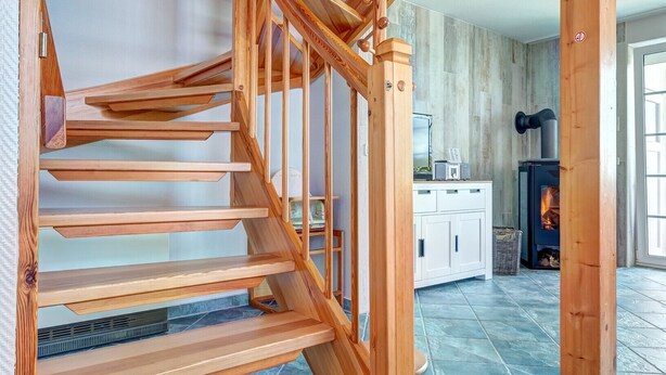 Un escalier en bois au design moderne, menant à une pièce dotée d’une cheminée et d’un sol carrelé.