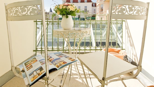 A balcony with a white metal chair, a small table with a vase of flowers, and a magazine.