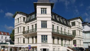 A large, white, multi-story building with a prominent tower and balcony.