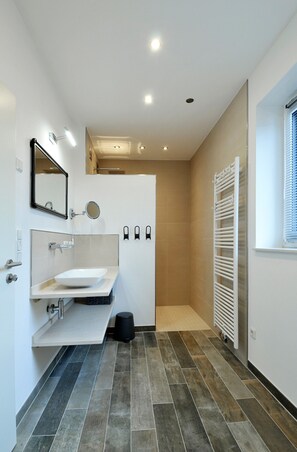Features a sleek vanity with a large sink and mirror, a beige shower area, and a towel rack.