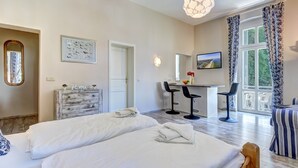 A hotel room with two beds, a desk with two chairs, a large window with curtains, and a view of greenery outside. - Vacation apartment "Küstenwald" in the Zinnowitzer Hof on Usedom! (Zinnowitz)