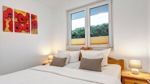 Un dormitorio con una cama, dos mesitas de noche, un ventanal con persianas y tres cuadros en la pared.