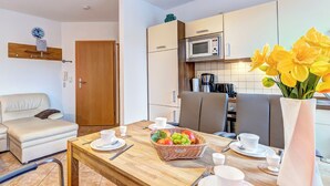 Un espacio habitable compacto con kitchenette, una zona de comedor con una mesa para dos, un sofá y un florero con flores.