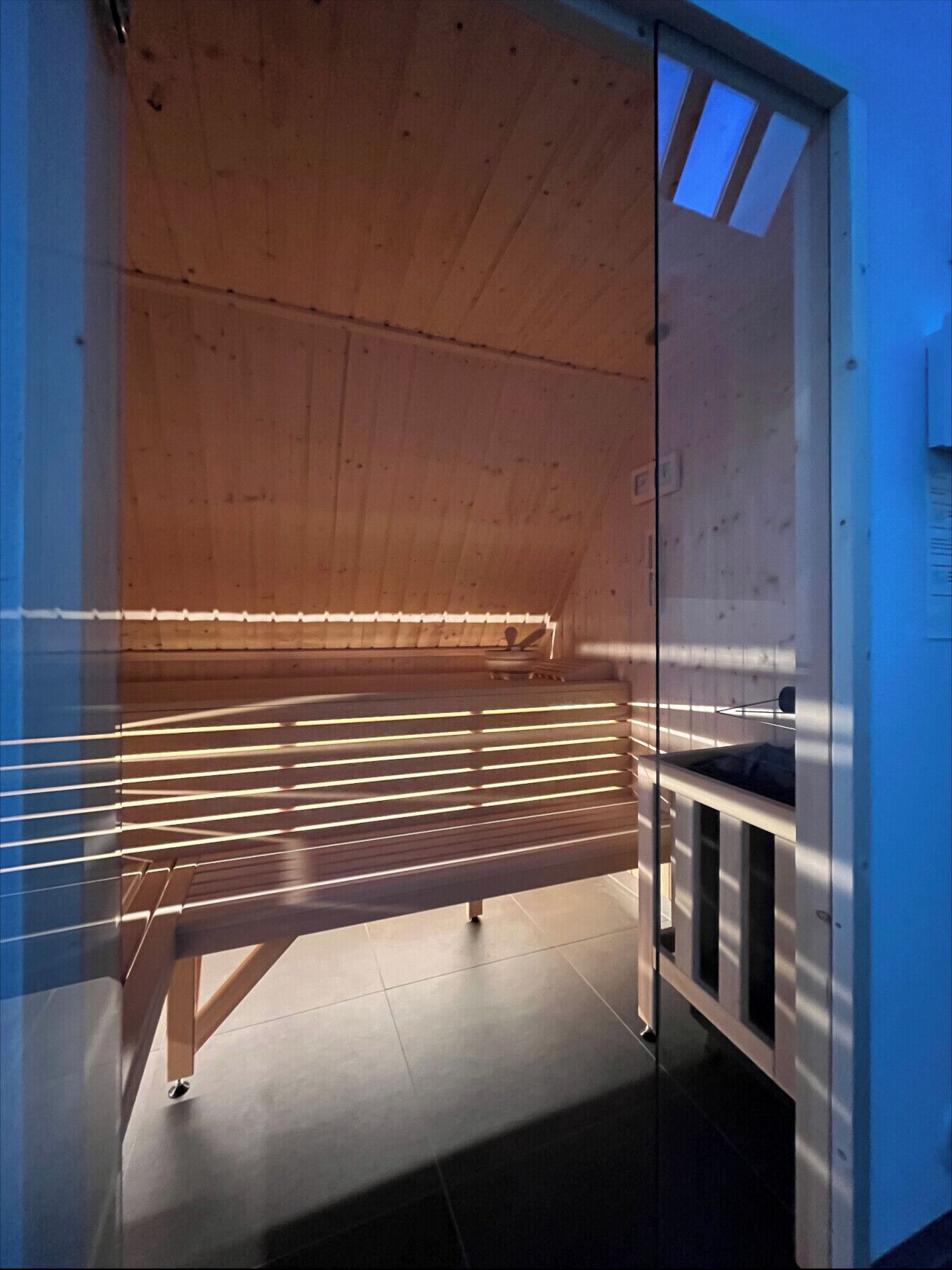A room with a wooden ceiling, a bench, and a skylight.