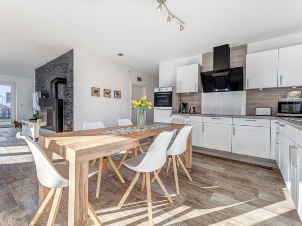 A modern kitchen with white cabinets, a wooden dining table, and a black range hood. - Villa Maarten in Zempin: 500 m to the sandy beach, sauna & WLAN for families (Zempin)