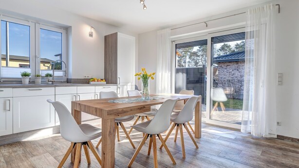 Una cocina moderna con armarios blancos, una mesa de comedor de madera con cuatro sillas y un amplio ventanal con vistas al exterior.