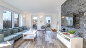 Una sala de estar moderna con un sofá gris, una mesita de centro blanca y un televisor en una pared de piedra.