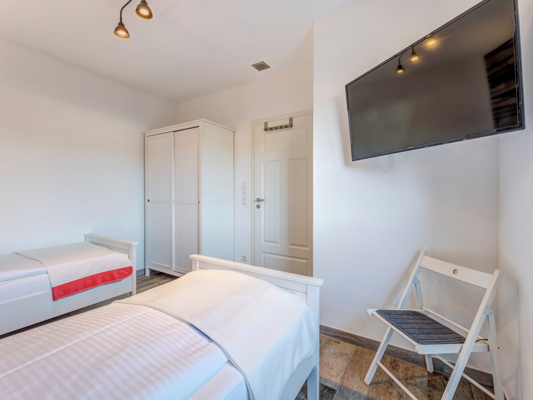 A bedroom with two beds, a wardrobe, a TV, and a chair.