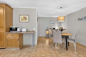 A modern kitchen with a microwave, toaster, and wooden cabinets. There is a dining area with a table, chairs, and a pendant light.