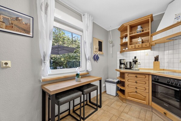 Kompakti keittiö, jossa on puinen työtaso, sisäänrakennettu uuni ja ikkuna, josta avautuu näkymä vehreään maisemaan.