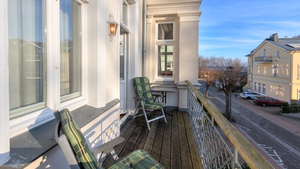 Ein Balkon mit zwei Sesseln in Grün-Karomuster, einem Tisch und einer Lampe.