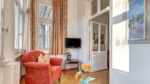 Ein gemütliches Wohnzimmer mit einem roten Sessel, einem Flachbildfernseher und einer Vase mit Blumen.