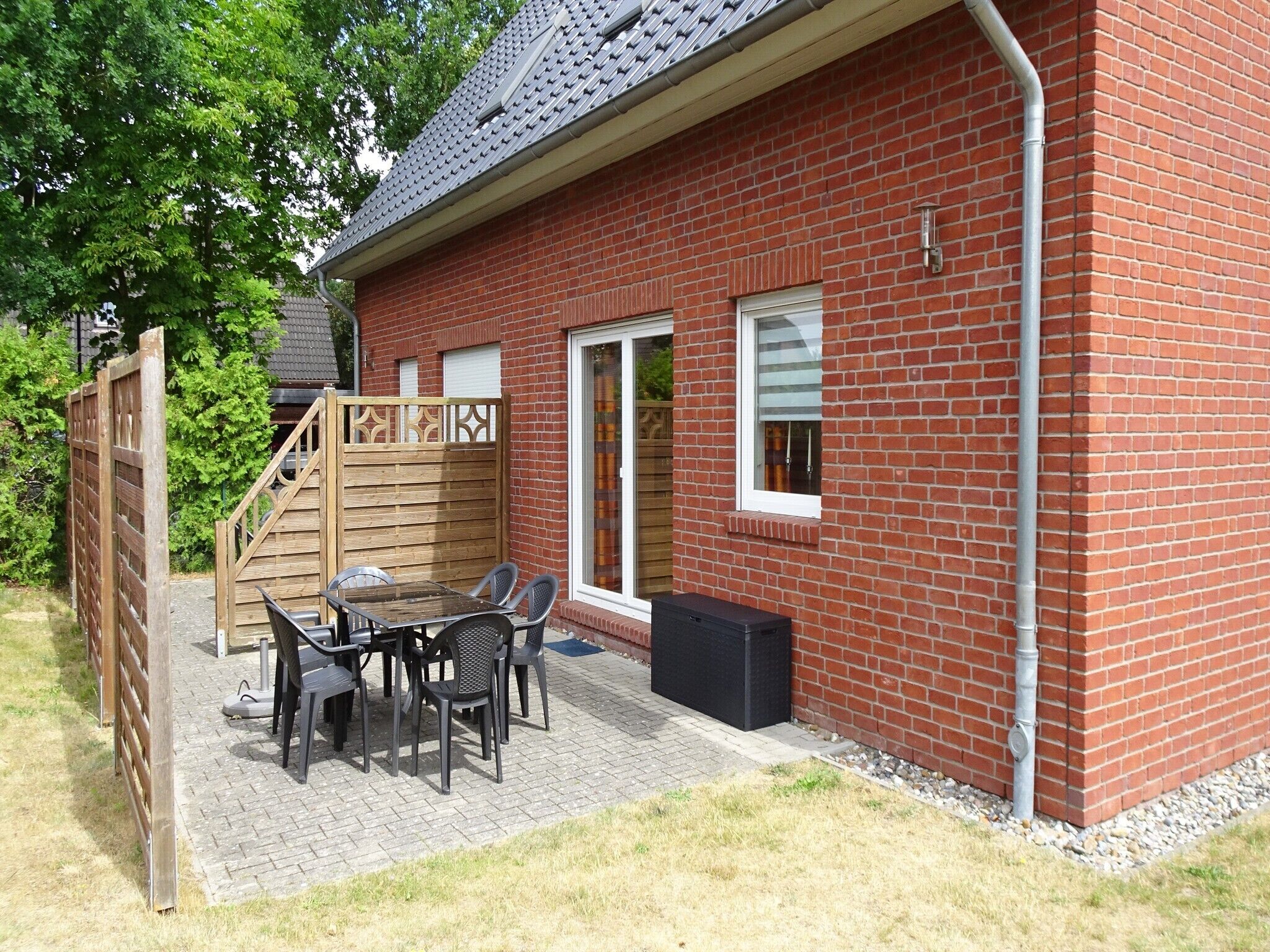Ein Ziegelhaus mit Terrasse, einer Holzspielanlage und einem Tisch mit Stühlen.