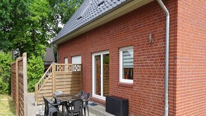 Une maison en briques avec un patio, une structure de jeu en bois et une table avec des chaises.