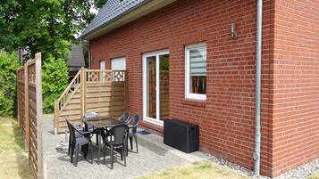 Ein Ziegelhaus mit Terrasse, einer Holzspielanlage und einem Tisch mit Stühlen.