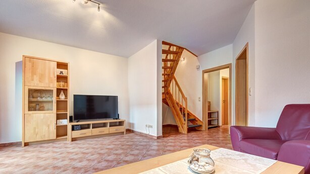Un salon avec un meuble TV en bois, un canapé et un escalier.