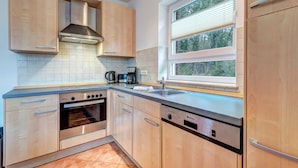 Une cuisine moderne avec des meubles en bois, un four encastré, un lave-vaisselle et une fenêtre avec des stores.