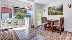 A dining area with a wooden table and chairs, a large window, and a painting on the wall. - Vacation home Schwalbennest with terrace, WLAN and close to the sandy beach in Kölpinsee (Kölpinsee)