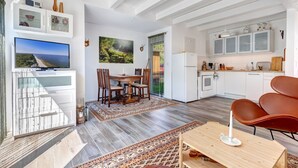 A spacious living area with a dining table, a TV, and a kitchen area with cabinets and a refrigerator. - Vacation home Schwalbennest with terrace, WLAN and close to the sandy beach in Kölpinsee (Kölpinsee)