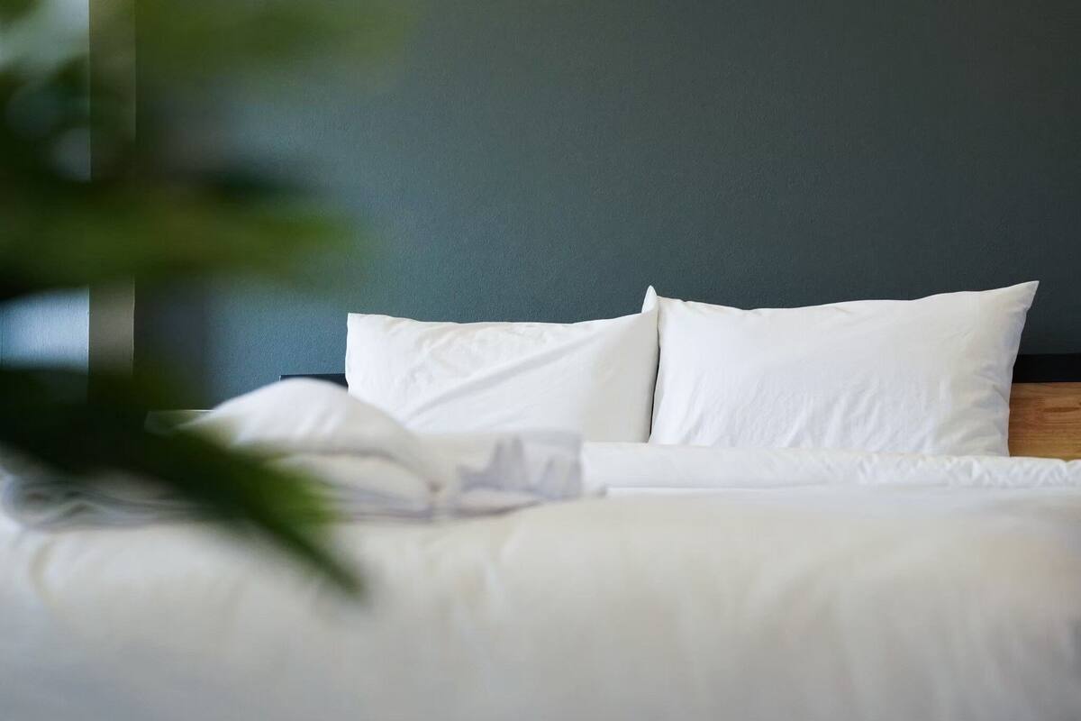 A neatly made bed with white bedding and pillows against a dark wall.