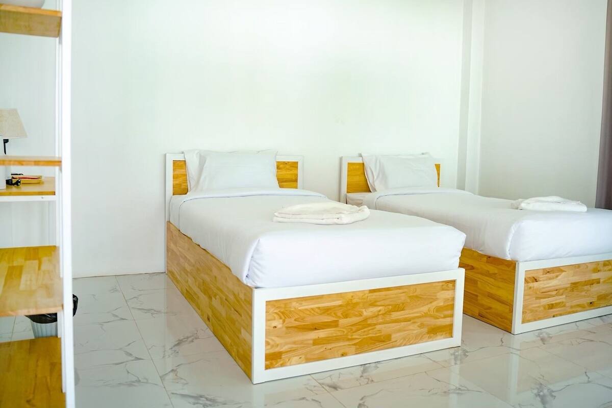 A hotel room with two beds, wooden headboards, white bedding, and a marble floor.