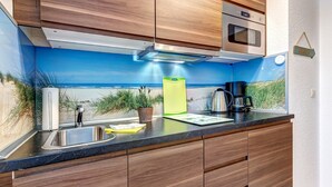 Uma cozinha moderna com armários de madeira, uma pia de aço inoxidável e vista para a praia através de um mural.