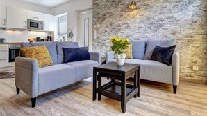 A modern living room with two grey sofas, a small dark wooden table, and a stone wall.