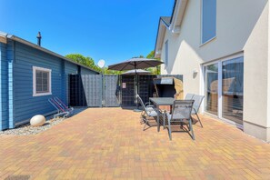 Een terras met een tafel, stoelen, een barbecue en een overdekte zithoek.