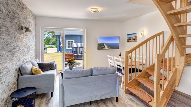 A modern living room with a grey sofa, a wooden staircase, and a view of the outdoors.