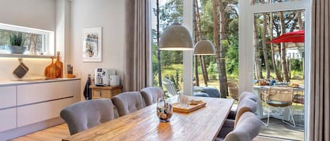 Enjoy meals in the dining area with a long table and comfortable seating, surrounded by a lush garden view.