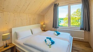A wooden cabin bedroom with two beds, a window with curtains, a nightstand with a lamp, and a radiator. - "Söt Mine" Seaside Cottage – a stylish retreat on the Baltic Sea for up to 7 people (Loddin OT Stubbenfelde)