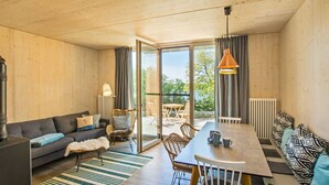A cozy living area with a sofa, dining table, and chairs, a fireplace, and a view through large glass doors. - "Söt Mine" Seaside Cottage – a stylish retreat on the Baltic Sea for up to 7 people (Loddin OT Stubbenfelde)